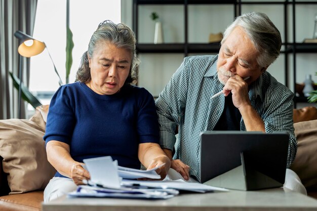 Ernsthaftes gestresstes asiatisches älteres altes Ehepaar, das sich Sorgen um Rechnungen macht, bespricht unbezahlte Bankschuldenpapiere traurige arme Familie im Ruhestand, die sich Sorgen um Geldprobleme macht