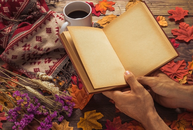 Ernten Sie die Hände, die Buch nahe Kaffee und Blumen halten