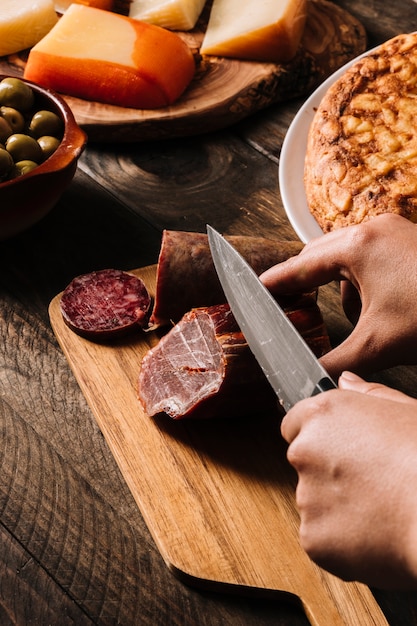 Ernten Sie die Hände, die geräuchertes Fleisch nahe Lebensmittel schneiden