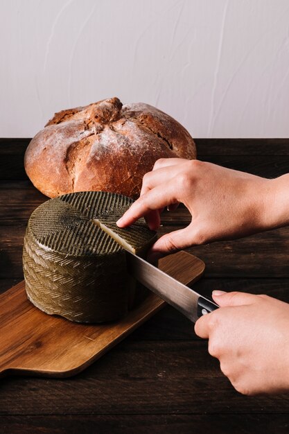 Ernten Sie die Hände, die Käse nahe Brot schneiden
