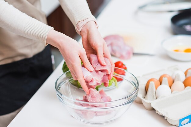 Ernten Sie die Hände, die rohes Fleisch in Platte setzen