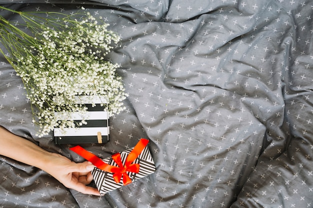 Ernten Sie die Hand, die Geschenk nahe Blumenstrauß und Notizbuch hält