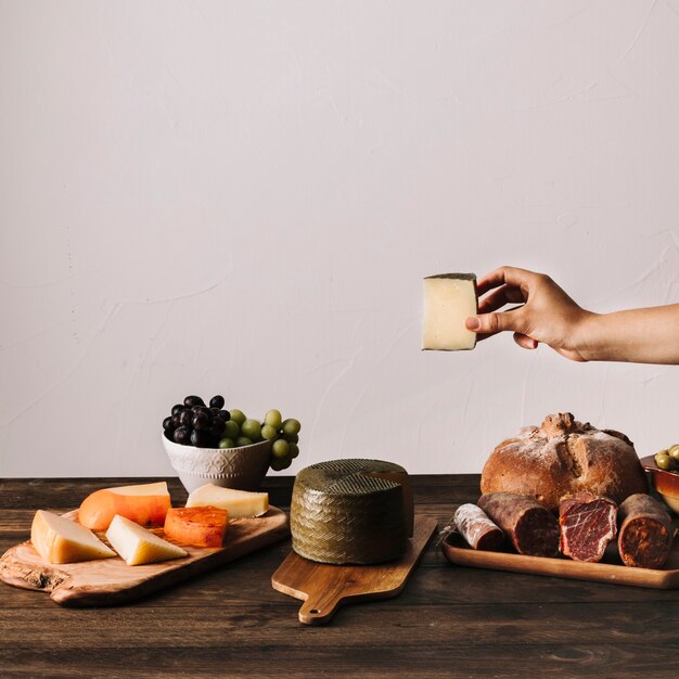 Ernten Sie die Hand, die Käse über Tabelle mit Nahrung hält