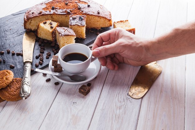 Ernten Sie die Hand, die Kaffee nahe Kuchen nimmt