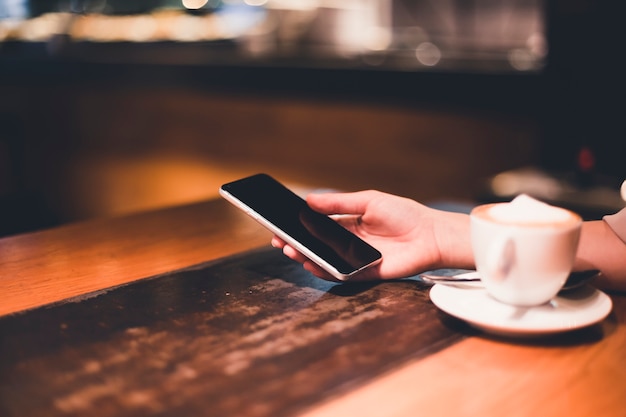 Kostenloses Foto ernten sie die hand, die smartphone nahe kaffee hält