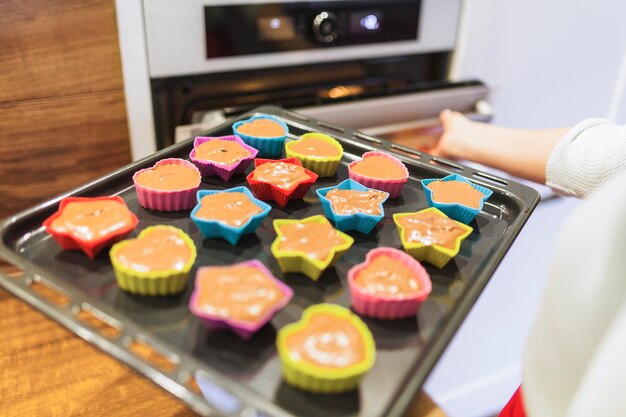 Ernten Sie die Person, die kleine Kuchen in Ofen setzt