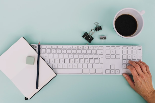 Ernten Sie Hand unter Verwendung der Tastatur nahe Briefpapier und Kaffee