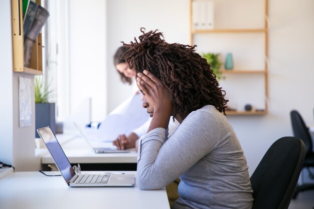 Erschöpfte Afroamerikanerfrau, die Laptop betrachtet