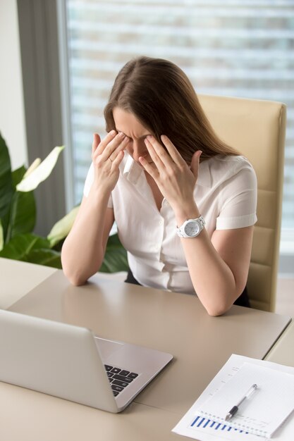 Erschöpfte Geschäftsfrau, die am Schreibtisch im Büro sitzt