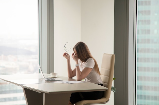 Erschöpfte Geschäftsfrau, die im Büro sitzt