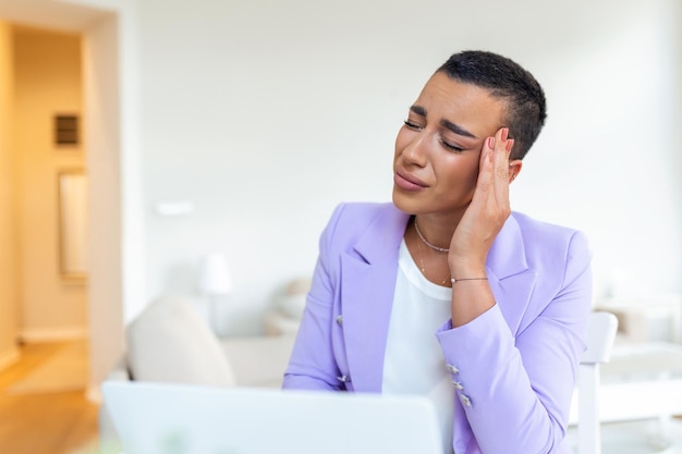 Erschöpfte Geschäftsfrau mit Kopfschmerzen im Home Office Afroamerikanische kreative Frau, die am Schreibtisch arbeitet und sich müde fühlt Gestresste Geschäftsfrau, die Augenschmerzen bei Überarbeitung verspürt