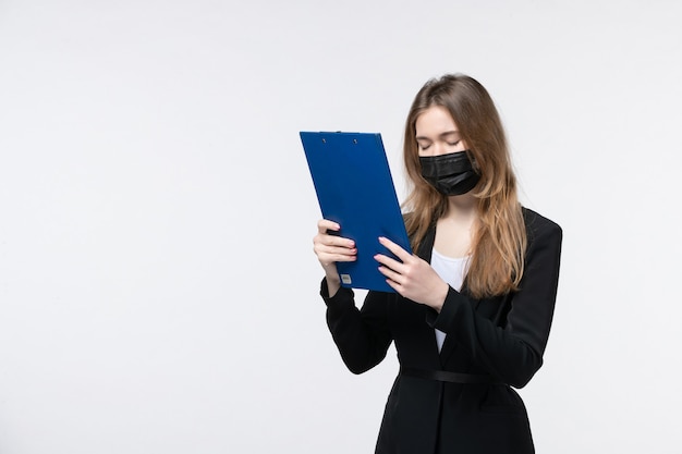 Erschöpfte Unternehmerin im Anzug, die ihre medizinische Maske trägt und Dokumente mit Kopfschmerzen auf Weiß aufhebt
