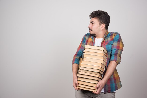 Erschöpfter Student mit Stapel Büchern, die irgendwo schauen