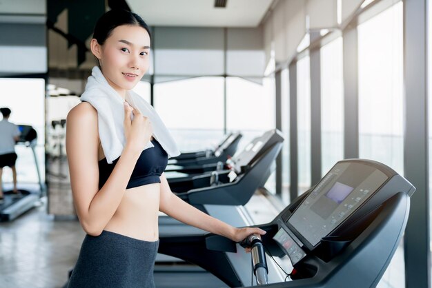 Erschöpftes asiatisches Mädchen, das auf dem Laufband im Fitnessstudio steht, entspannt sich und kühlt gesunde Ideen ab