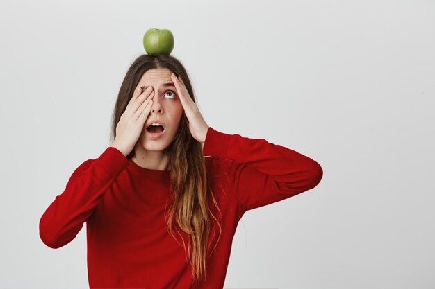 Erschrockene und nervöse süße Frau, die Apfel auf ihrem Kopf, offenem Mund und Keuchen prüft