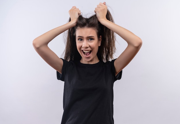 Erschrockenes junges kaukasisches Mädchen, das schwarzes T-Shirt trägt, packte Haare auf lokalisiertem weißem Hintergrund