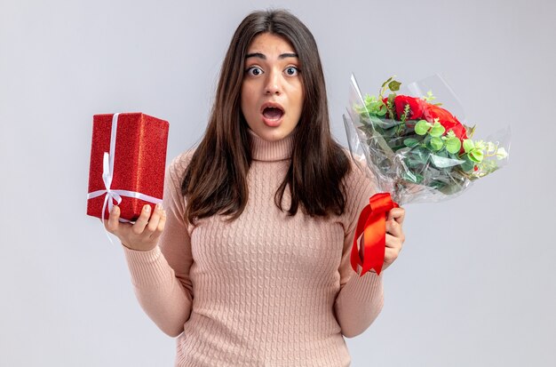 Erschrockenes junges Mädchen am Valentinstag mit Geschenkbox mit Blumenstrauß isoliert auf weißem Hintergrund