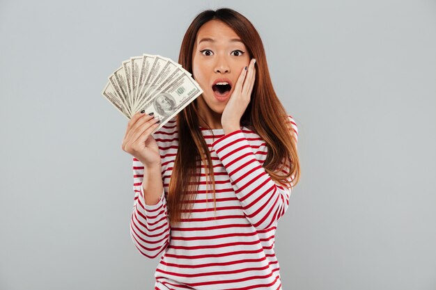 Erstaunlich schockierte junge asiatische Dame, die Geld hält.