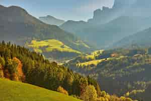 Kostenloses Foto erstaunliche herbstlandschaft im dorf santa maddalena mit bunten kirchenbäumen und wiesen unter aufgehenden sonnenstrahlen dolomiten italien