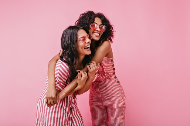 Erstaunliche, schöne Dame freut sich und genießt Fotoshooting in Pink. Afrikanische Mädchen mit lockigem Haar in der Sonnenbrille lachen.