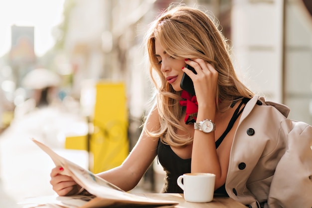 Erstaunliches blondes mädchen, das nachrichten mit freund bespricht, während es am telefon spricht