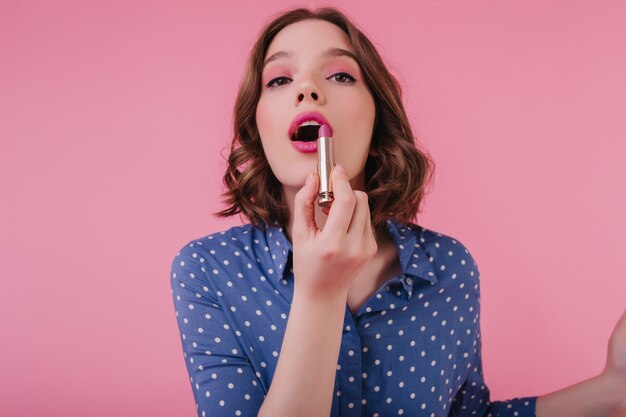 Erstaunliches braunhaariges Mädchen, das Lippenschminke tut. süße Dame mit rosa Lidschatten mit Lippenstift.