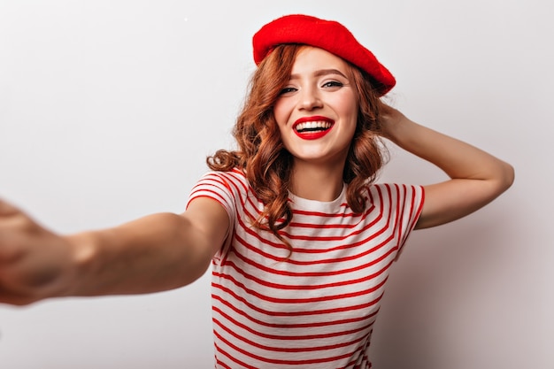 Erstaunliches europäisches Mädchen in der roten Baskenmütze, die positive französische junge Frau lacht, die selfie macht.