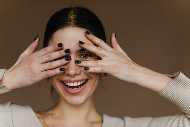 Erstaunliches Mädchen mit Party Make-up posiert mit glücklichem Lächeln. Nahaufnahmeporträt der frohen jungen Dame mit schwarzen Haaren.