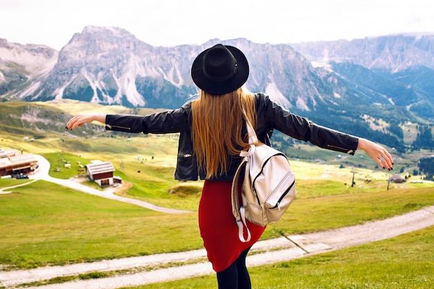 Kostenloses Foto erstaunliches reiseerlebnisbild der schönen stilvollen frau, die zurück aufwirft und den atemberaubenden blick auf die berge, reise in den italienischen dolomiten betrachtet. hipster-mädchen, das abenteuer genießt.