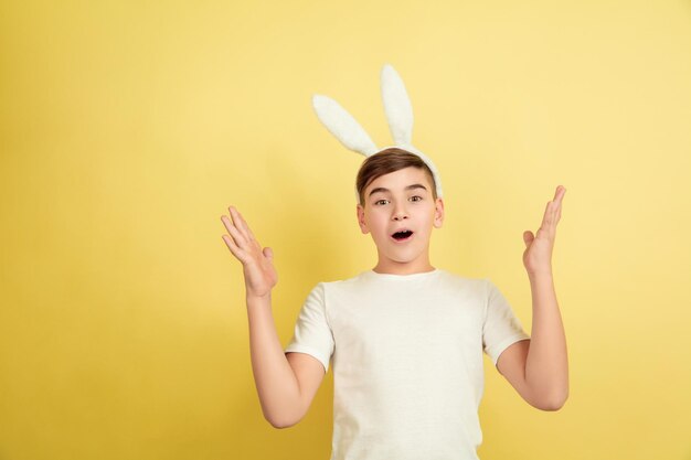 Erstaunt, geschockt. Kaukasischer Junge als Osterhase auf gelbem Studiohintergrund. Fröhliche Ostergrüße.