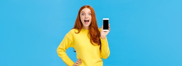 Kostenloses Foto erstaunte und beeindruckte aufgeregte rothaarige frau im gelben pullover stellt neue app vor, die smartpho zeigt