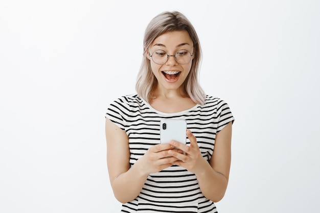 Erstauntes blondes Mädchen, das im Studio mit ihrem Telefon aufwirft