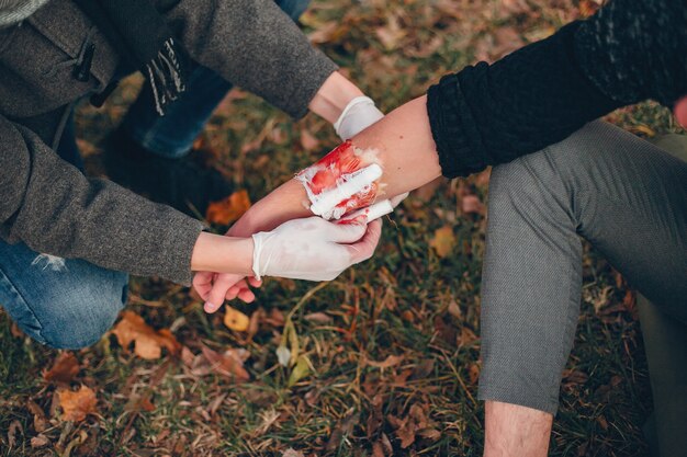 Erste Hilfe im Park leisten. Mann bandagierte verletzten Arm. Guy hilft einem Freund.