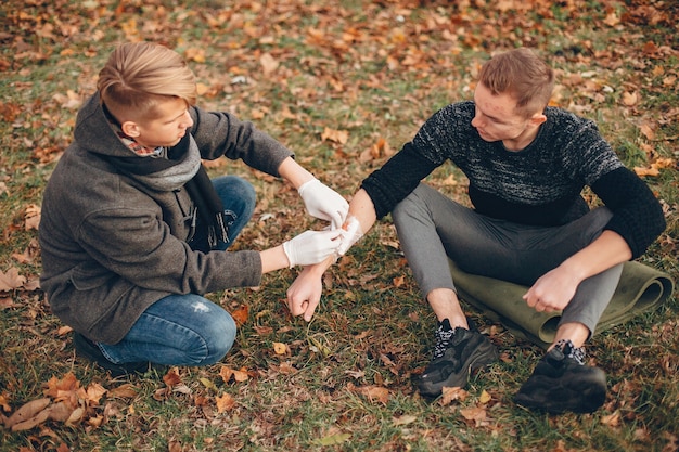 Erste hilfe im park leisten. mann bandagierte verletzten arm. guy hilft einem freund.