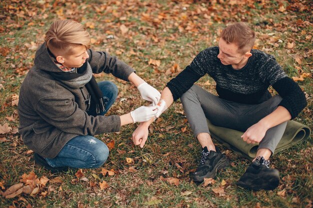 Erste Hilfe im Park leisten. Mann bandagierte verletzten Arm. Guy hilft einem Freund.