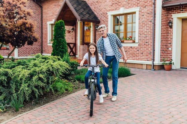 Erste Lektionen Radfahren Reiten. Hübscher Großvater unterrichtet seine Enkelin dagegen.