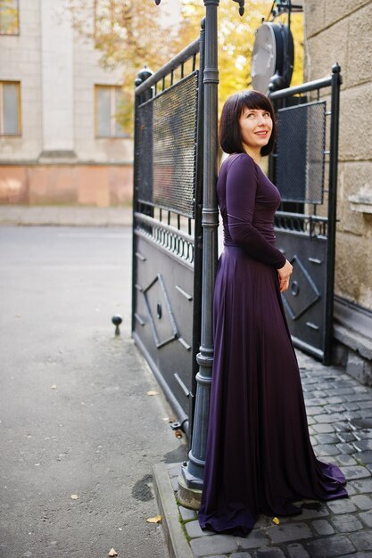 Erwachsene Brünette Frau am violetten Kleid Hintergrund schwarze Eisentore