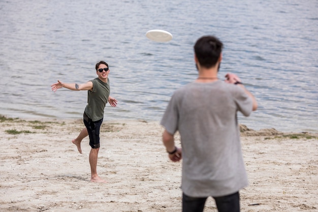 Kostenloses Foto erwachsene männer, die frisbee auf ufer während der feiertage spielen