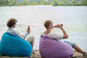 Kostenloses Foto erwachsene männer, die mit bier nahe wasser sich entspannen