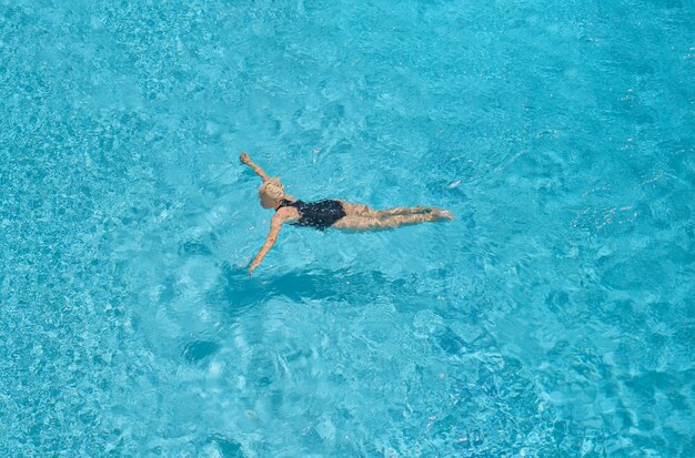 Erwachsene schöne Frau in einem schwarzen Badeanzug schwimmt in einem blauen Pool, Freizeit- und Urlaubszeit, Vogelperspektive auf den Pool, Draufsicht