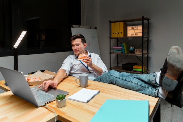 Erwachsener Arbeiter, der Pizza während der Arbeit von zu Hause aus hat