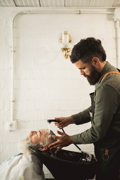 Erwachsener Friseur, der Haar des alten Mannes auf Rückspülung wäscht