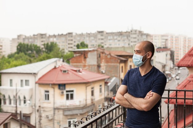 Erwachsener Mann auf Balkon mit Gesichtsmaske während der globalen Pandemie.