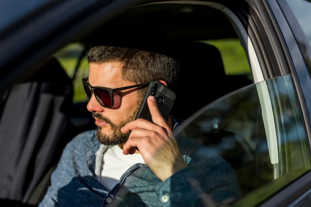 Erwachsener Mann, der im Auto sitzt und am Telefon spricht