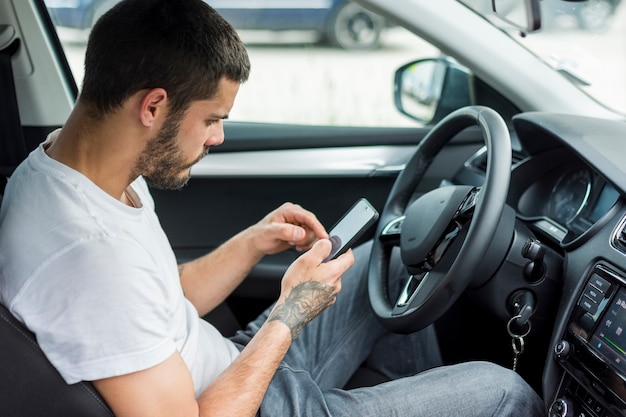Erwachsener Mann, der im Auto sitzt und Smartphone verwendet