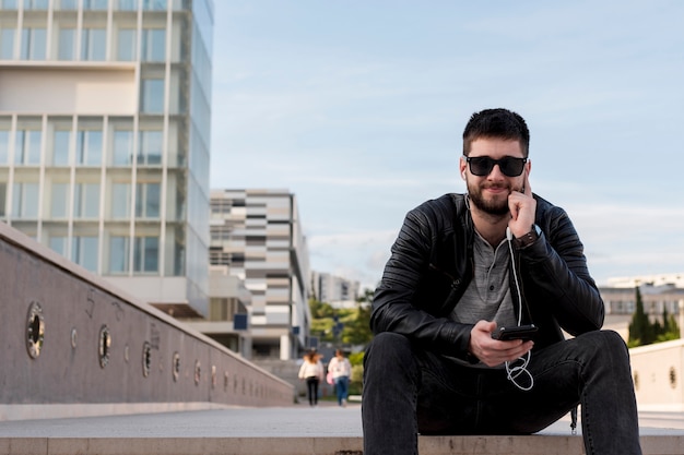 Kostenloses Foto erwachsener mann, der in der hand auf pflasterung mit smartphone sitzt