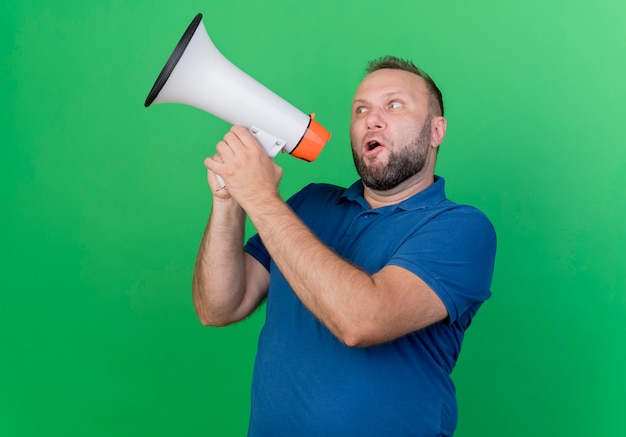 Erwachsener slawischer Mann, der Seite betrachtet, die durch Sprecher lokalisiert auf grüner Wand spricht