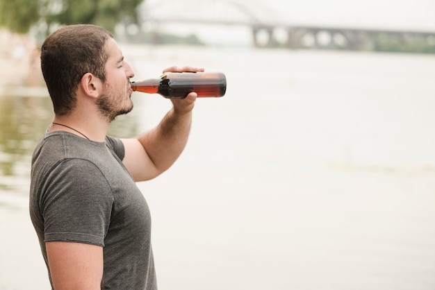 Erwachsenes Manntrinkendes Bier nahe Wasser