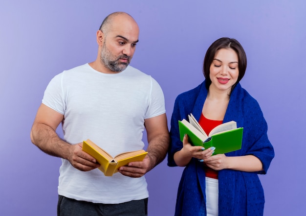 Erwachsenes Paar erfreute Frau eingewickelt in Schal, das Buch liest, beeindruckte Mann, der Buch hält und ihr Buch betrachtet