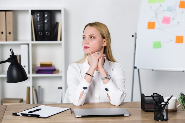 Erwogene blonde junge Geschäftsfrau, die am Arbeitsplatz im Büro sitzt